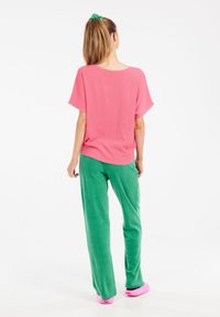 Maglietta rosa a coste con maniche corte, abbinata a pantaloni della tuta verdi e scarpe slip-on rosa. Design semplice con una vestibilità rilassata.