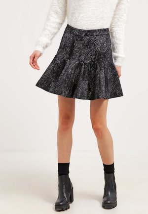 Femme portant une jupe évasée texturée noir et blanc, des bottines noires à talons carrés et un pull à manches longues blanc et duveteux.