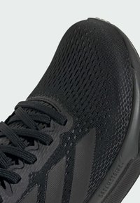 Scarpe sportive nere con una tomaia in maglia lavorata, lacci piatti e tre strisce diagonali sui lati. Presentano una punta arrotondata e una suola imbottita.