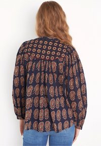 Blusa blu navy con un motivo paisley, caratterizzata da una parte superiore arricciata, maniche arricciate e una vestibilità comoda. Il tessuto testurizzato aggiunge profondità.