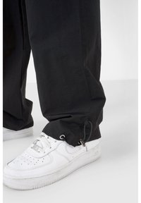 Pantaloni neri larghi con un sistema di regolazione alla caviglia, abbinati a sneakers bianche basse con dettagli perforati.