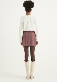 Top bianco a maniche lunghe con scollo arricciato abbinato a una mini gonna a scacchi color bordeaux. Stivali alti fino al ginocchio color crema completano l'outfit.