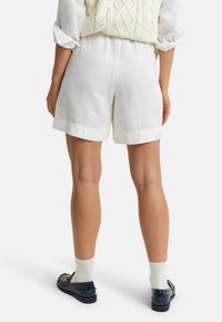 Witte linnen shorts met een relaxte pasvorm, voorzien van een omgerolde zoom. Draagt een crèmekleurige kabeltrui en marineblauwe instappers met witte sokken.