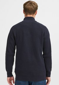 Marineblauer, gerippter Strickpullover mit hohem Kragen, langen Ärmeln und einer strukturierten Oberfläche. Seitliche Schlitze am Saum.