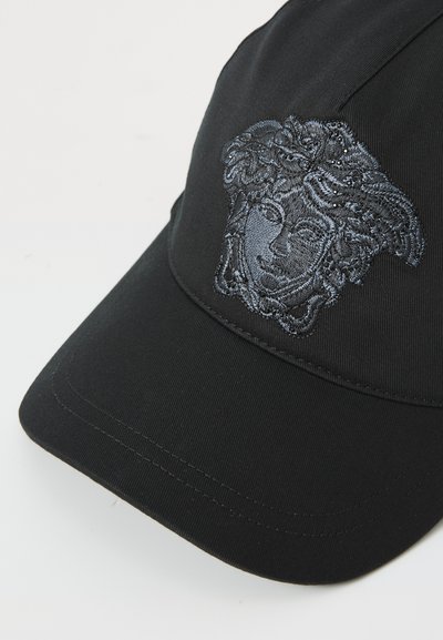 Casquette noire avec un design brodé d'un visage sur le devant. Texture lisse avec une visière courbée et des détails de couture visibles.