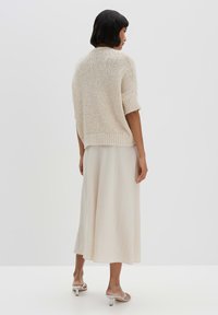 Pull en crème tricoté à manches courtes, associé à une jupe fluide de couleur beige clair. Textures lisses, coupe décontractée, porté avec des sandales à talons neutres.