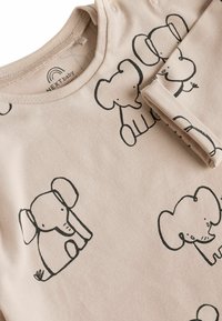 Pitkähihaisen vaaleanbeiget bodysuit, jossa on mustia norsujälkiä, pyöreä pääntie ja napsautettavat kiinnitykset olkapäällä helpompaa pukemista varten.