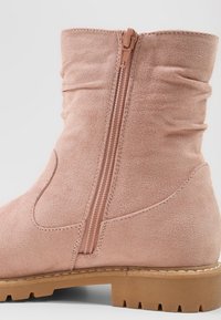 Světle růžová koženka na kotníky se skládacím designem, boční zip a světle hnědá gumová podrážka s texturovaným vzorem. 