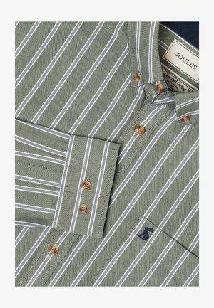 Rohelise triibulise särgi valgete triipudega, millel on pruunid nupud, terav krae ja väike tumesinine logo taskul.