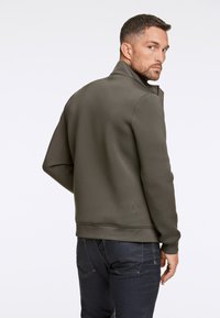 Olijfgroene sweatshirt met een hoge kraag, textuurmateriaal en ribgebreide boorden. Gecombineerd met donkere jeans, die een slim fit ontwerp laten zien.