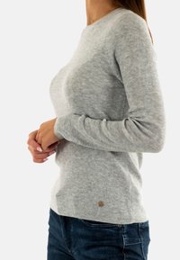 Maglione a coste grigio chiaro realizzato in materiale morbido, con maniche lunghe e un design leggermente aderente. Accento del logo ben visibile sull'orlo.