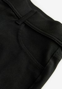 Țesătură din denim negru cu textură în relief. Prezintă un buzunar frontal și bucle pentru brâu. Cusuturi curate pe întreaga suprafață, cu un design minimal.