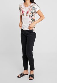 Top corto de manga corta con estampado floral en color claro, combinado con pantalones negros de corte slim y sandalias negras sin talón con tachuelas. Textura de tela suave.