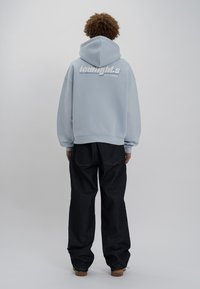 Felpa leggera blu chiaro con una grande grafica bianca sul retro, abbinata a pantaloni in denim scuro. Il tessuto sembra morbido e ha una vestibilità comoda.