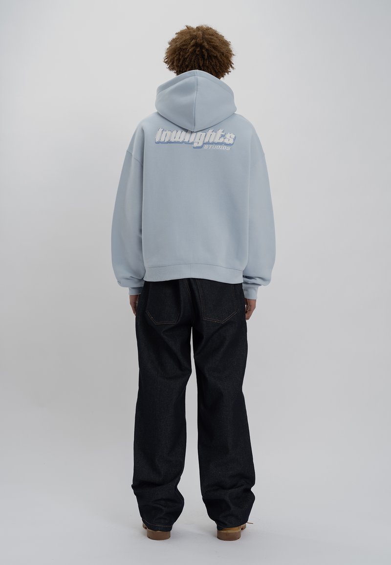 Felpa leggera blu chiaro con una grande grafica bianca sul retro, abbinata a pantaloni in denim scuro. Il tessuto sembra morbido e ha una vestibilità comoda.