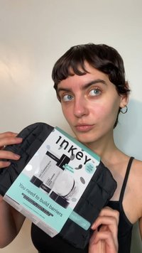 Pochette noire à texture matelassée, contenant des produits de soin de la peau. L'emballage présente le nom de la marque "The Inkey List", avec un accent turquoise et un texte d'instructions.