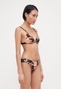 Ensemble de bikini floral avec un fond noir orné de fleurs orange et crème. Le haut a des bonnets triangulaires et des bretelles fines ; le bas est taille basse.
