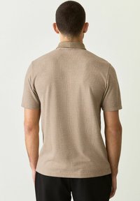 Polo de manga corta hecho de un tejido beige texturizado con un patrón de cuadros sutil y un cuello, que presenta un dobladillo recto y un ajuste relajado.