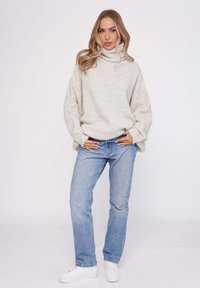 Hellegrauer, gerippter Strickrollkragenpullover mit übergroßen Ärmeln, kombiniert mit blauen, geraden Jeans und weißen Sneakern.