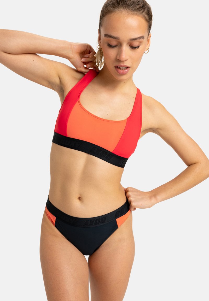 Röd och orange tvåfärgad bikiniöverdel med en svart remsor som har logotypen. Underdelen är svart med orange detaljer. Tillverkad av stretchigt tyg.