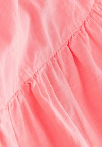 Tejido de coral con un acabado suave y texturizado. Presenta pliegues en la costura, creando una apariencia fluida y en capas.