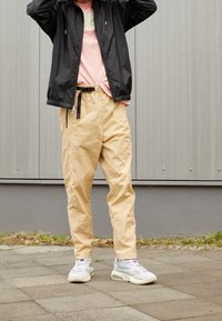Svart zip-up jacka, rosa t-shirt med logotyp, beige byxor och grå-vita sneakers. Texturerat tyg och avslappnad passform.