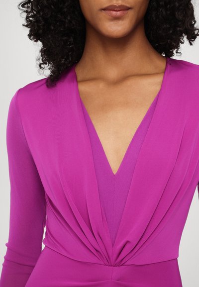 Φούξια φόρεμα με βαθύ V ντεκολτέ, μακριά μανίκια και συγκεντρωμένες λεπτομέρειες στη μέση. Λείο, ελαστικό ύφασμα με υφή.