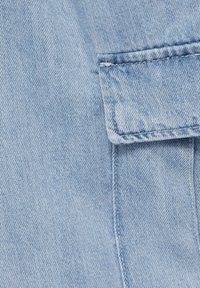 Tissu en denim bleu clair avec texture de tissage visible et un rabat de poche rectangulaire avec détails de couture.