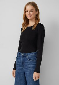 Maglietta nera a maniche lunghe con scollo tondo, abbinata a jeans blu a vita alta con gamba dritta e leggera scoloritura.