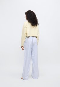 Κοντό κίτρινο φούτερ με μακριά μανίκια, σε συνδυασμό με ψηλόμεσο, ανοιχτό μπλε ριγέ παντελόνι με φαρδύ πόδι. Λείο ύφασμα, άνετη εφαρμογή.