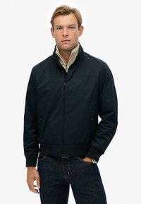 Chaqueta bomber de la marina con cremallera frontal, puños acanalados y bolsillos laterales. Presenta un cuello interior beige en contraste y una textura de tela suave.