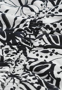 Tissu noir et blanc avec un motif floral abstrait, présentant un design texturé et froncé ainsi qu'une surface lisse sur un matériau doux.