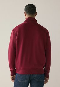 Burgundia fliisist pullover kõrge kraega, ribatud mansettide ja mugava lõikega. Omab siledat tekstuuri ja lihtsat disaini.