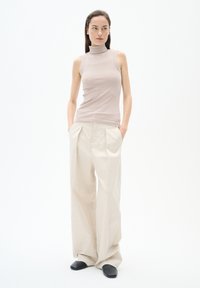 Top senza maniche in maglia a coste di un leggero beige abbinato a pantaloni larghi in crema. L'outfit presenta una vestibilità morbida e una texture sottile.