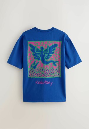 Blå bomulds t-shirt med et livligt grafisk design i grøn og pink, der skildrer en skikkelse med vinger og abstrakte mønstre.