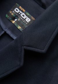 Tissu bleu marine foncé avec un gros plan d'un revers et une étiquette de vêtement à motif partiellement visible portant l'inscription « ombre ».