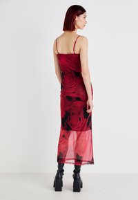 Vestido vermelho translúcido com padrão floral de rosas, alças finas e silhueta ajustada, atingindo a meia-perna, combinado com botas pretas até ao joelho.