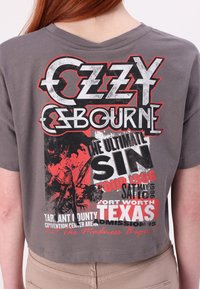 Gray cropped t-shirt featuring large graphic print with "Ozzy Osbourne," red and black accents, and event details from 1986 tour.