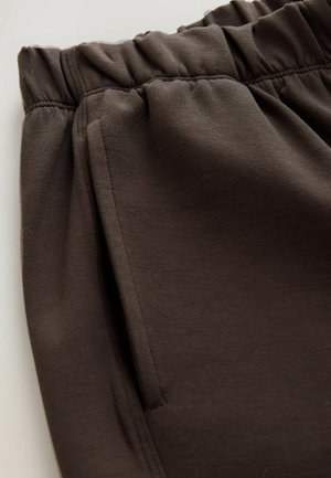 Braune Sweatpants mit elastischem Bund, ausgestattet mit einer Seitentasche und aus glattem Baumwollmischgewebe, in einer Nahaufnahme dargestellt.