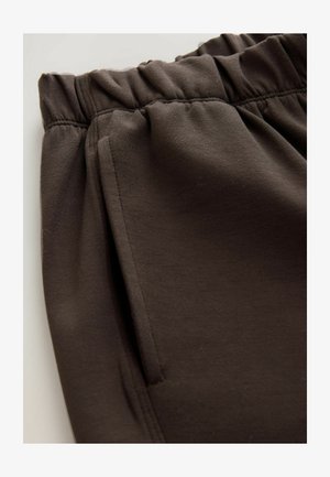 Bruine sweatpants met een elastische tailleband, voorzien van een zijzak en een soepel katoenmixmateriaal, getoond in een close-up zicht.