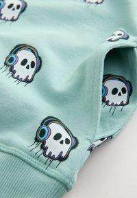 Tejido verde menta con diseños impresos repetidos de calaveras usando auriculares, con una textura suave y detalle de dobladillo acanalado.