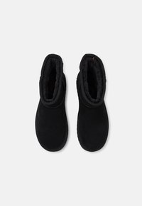Botas negras de ante hasta el tobillo con un forro suave y texturizado y acentos cosidos alrededor de la suela y la abertura. Diseñadas para la comodidad y el calor.
