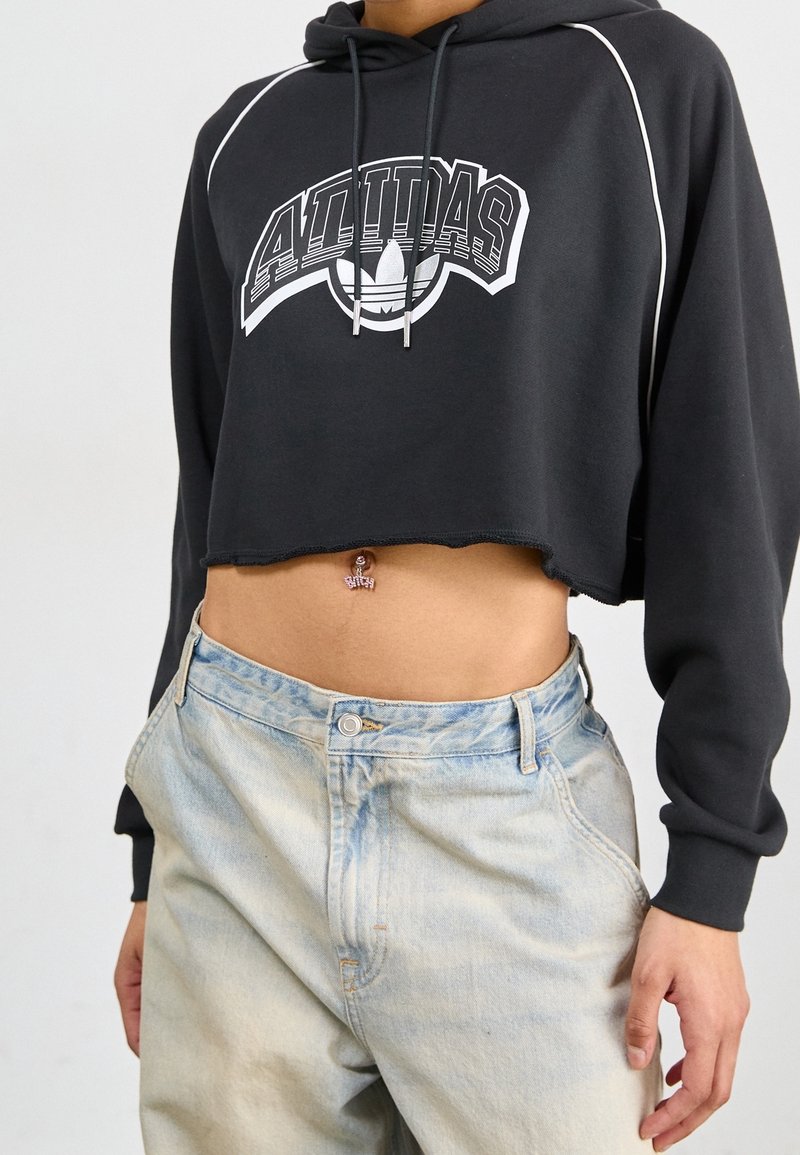 Czarna krótka bluza z kapturem z białym napisem "Adidas" i sznurkami, w połączeniu z jasnoniebieskimi jeansami z wysokim stanem i wyblakłą fakturą denimu.