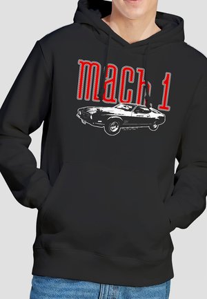 Schwarzer Kapuzenpullover mit rotem und weißem "Mach 1"-Schriftzug und Grafik eines klassischen Muscle-Cars, getragen von einer Person mit in den Taschen steckenden Händen.