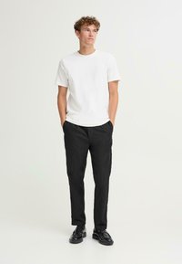 Bela bombažna majica, sproščen kroj, okrogla odprtina. Črne tapered hlače z žepi. Črne vezane čevlje. Preprost, sodoben outfit.