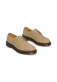 Scarpe in suede beige con punta rotonda, sei occhielli, lacci piatti e suola nera a contrasto con un dettaglio di cucitura gialla.