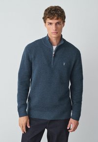 Granatowy sweter zapinany na zamek, wykonany z fakturowanej tkaniny, z prążkowanymi mankietami i dolnym wykończeniem, z małym logo na piersi oraz wysokim kołnierzem.
