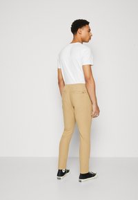 Light beige chinos with a slim fit, featuring two back pockets and a soft texture. Paired with a plain white t-shirt and black sneakers.