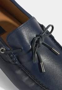 Marine lederen moccasinschoen met een gladde textuur, voorzien van een gestrikte detail en metallic aglets. Zichtbare stiksels langs de randen.