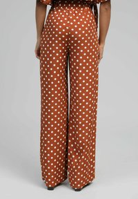 Pantalon large à pois marron, avec une taille élastique et une texture lisse, orné de grands pois blancs sur l'ensemble du tissu.